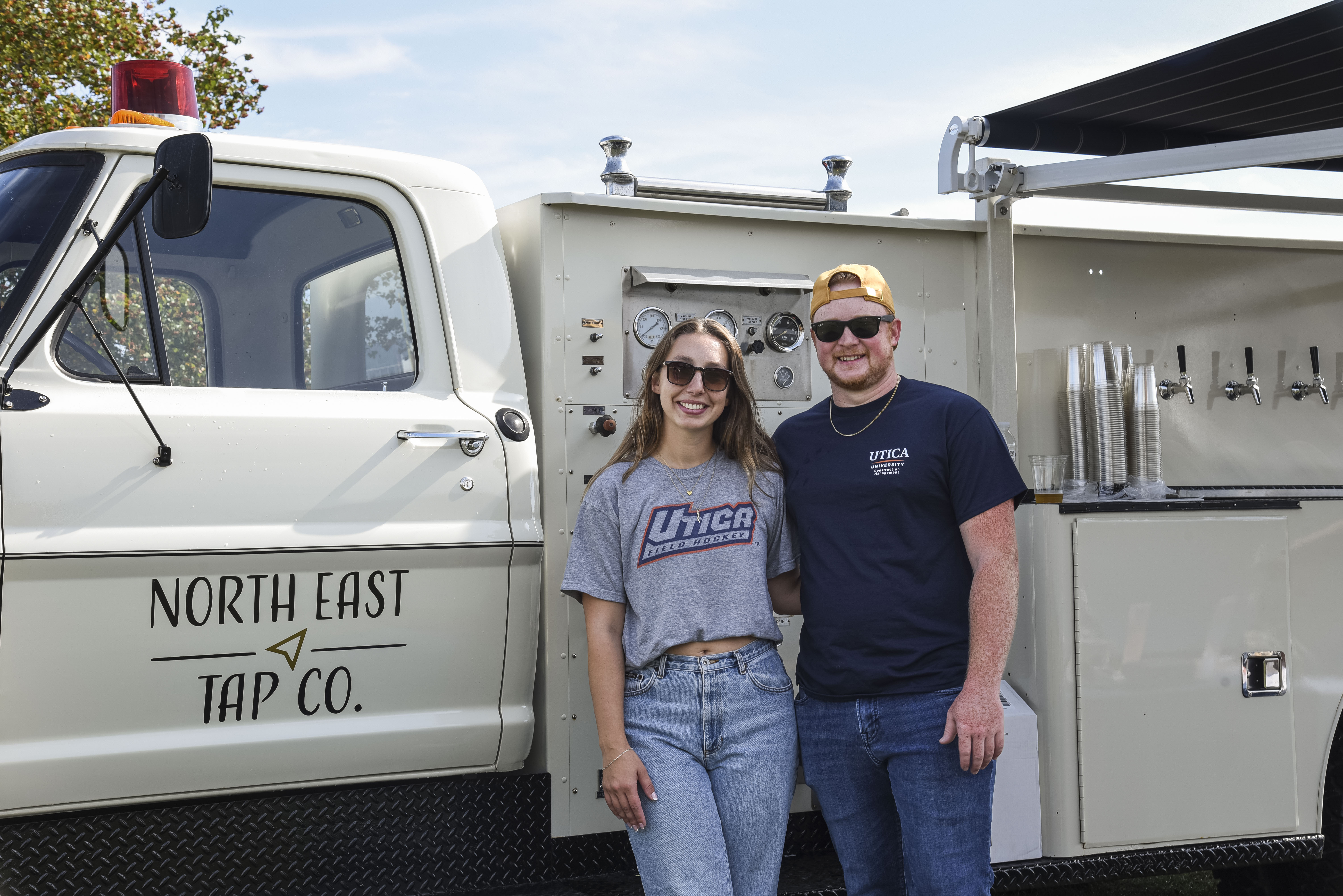 Abby D'Amato and Dawson Lagoe stand near their North East Tap Co. Beer Truck at Homecoming 2025