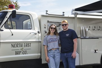 Abby D'Amato and Dawson Lagoe stand near their North East Tap Co. Beer Truck at Homecoming 2025